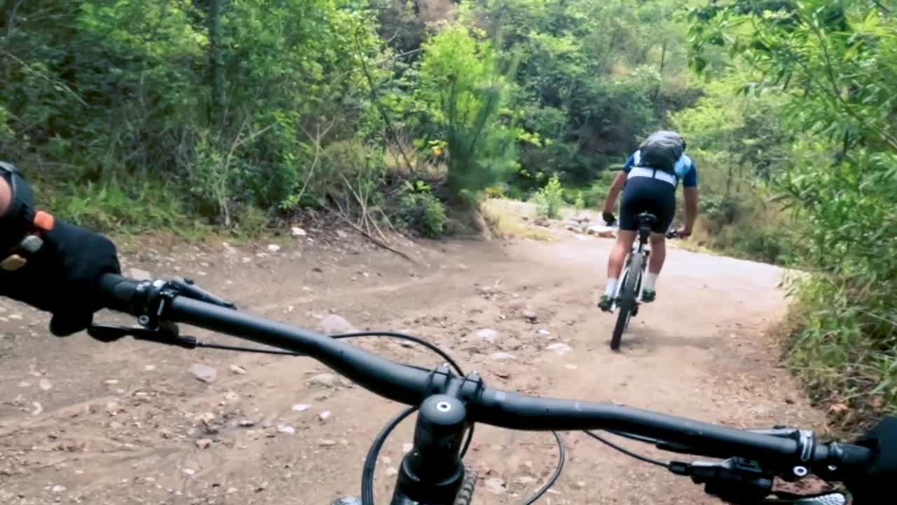 dos ciclistas andan en bicicleta por una carretera dentro de un bosque, una colina y un pueblo en guatemala, américa del norte