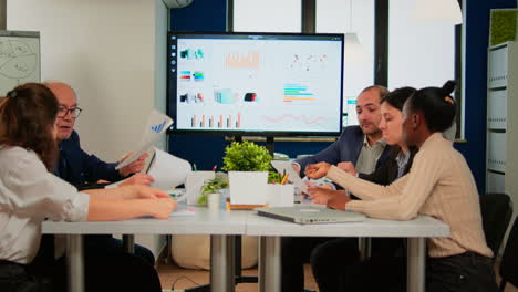 man leader pointing at digital interactive whiteboard sitting at brainstorming table