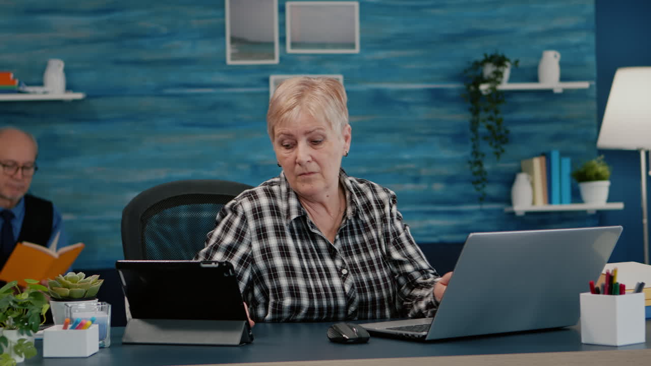 Multitasking retired woman reading on laptop and tablet in same time