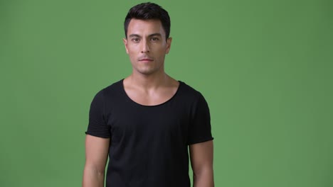 young handsome hispanic man against green background