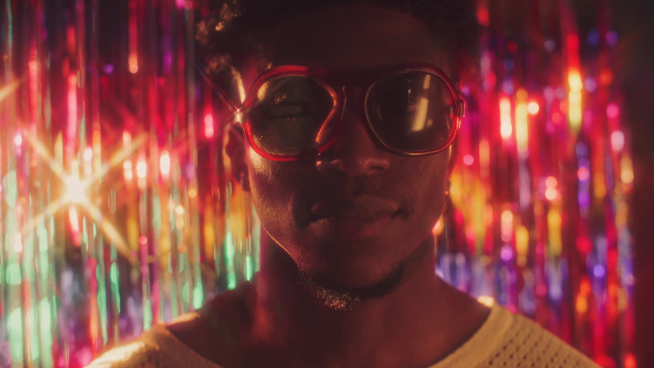 Portrait of Man in Sunglasses in Colorful Lights against Shiny Background