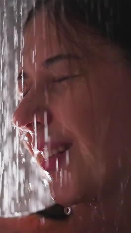 smiling woman in water sprays in shower closeup. pleasured brunette lady with closed eyes rests washing body in bathroom. recreation time at home