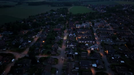 street with cars in american neighborhood at night. straight road leading to farm fields in distance. apartment blocks and houses in american city. aerial birds eye shot. peaceful neighborhood.