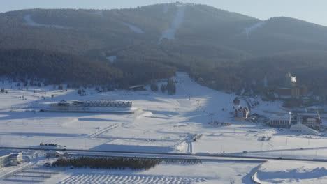 Ski-resort-with-slopes-on-alpine-tree-mountain-during-sunset-covered-in-snow