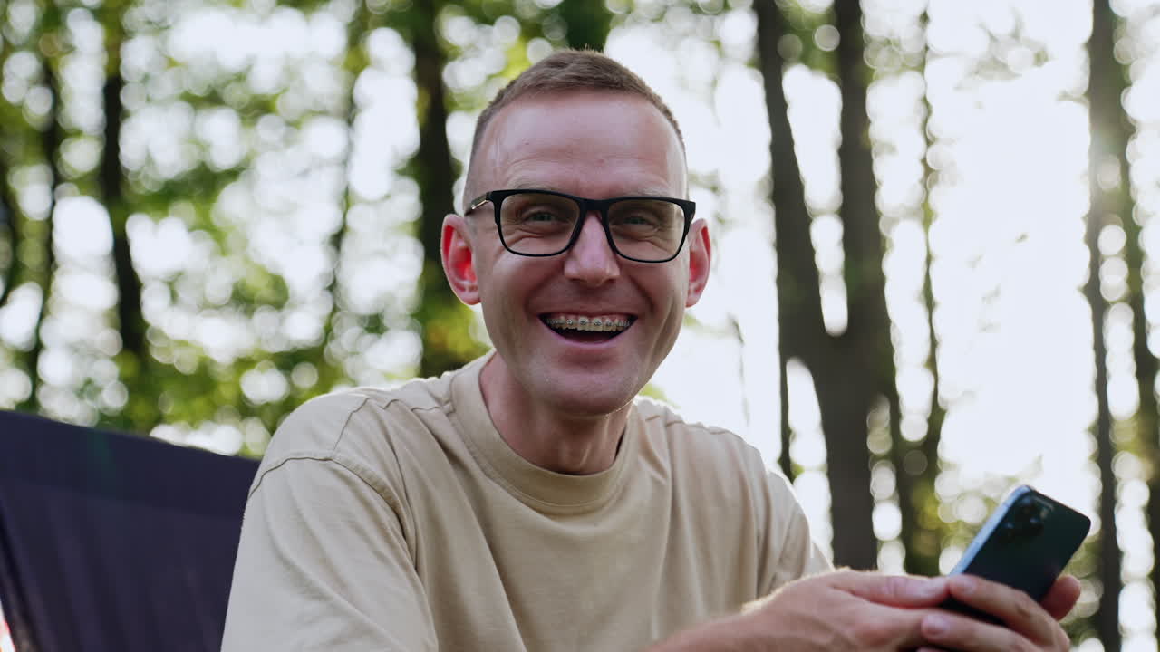 Smiling Caucasian man looks at his smartphone. Businessman receives a call and talk cheerfully looking at camera. Close up.