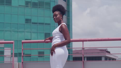 on a rooftop, a young black girl in a white dress gazes at the city