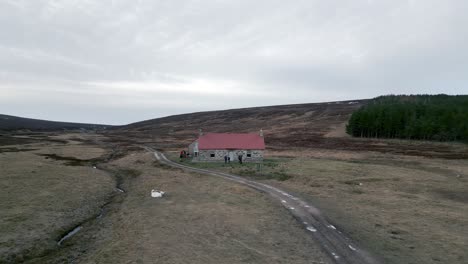 a drone flies backwards away from the red house bothy in the scottish highlands as people pack up bikes and talk outside the front door