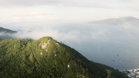 drone panning a cloudy peak of a tropical forest mountain in a summer day with the ocean on the background