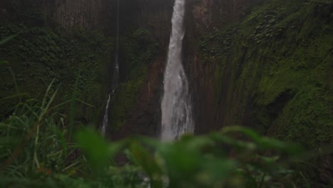 a stunning and powerful waterfall cascades down a sheer, rocky cliff face, surrounded by a dense, green rainforest