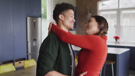 feliz pareja biracial abrazando y sonriendo juntos en la cocina
