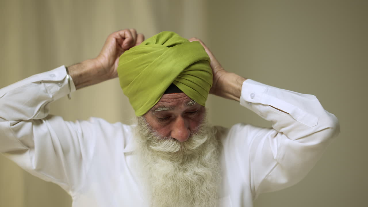 실시간으로 촬영된 평평한 배경에 터반을 착용할 때 살라이 바늘을 사용하는 수염을 가진 수석 시크 남자의 스튜디오