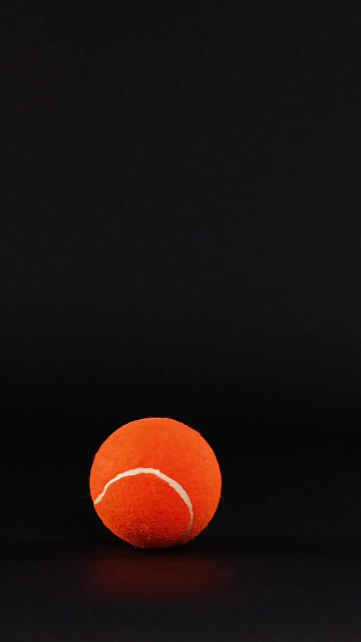 A tennis ball moves across a dark background