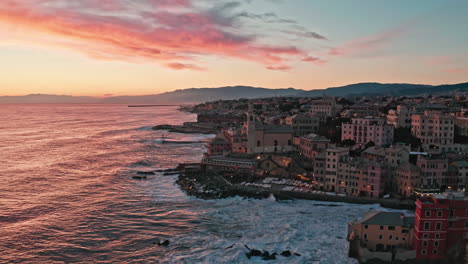 Boccadasse-in-Genoa-during-vibrant-sunset-as-waves-crash-into-coastline,-aerial