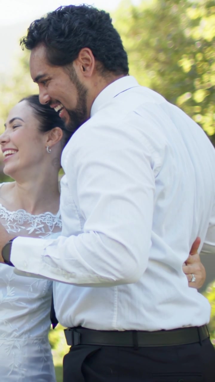 Video vertical: Copas de champán en alto, pareja vestida de novia abrazándose, mostrando anillo en jardín