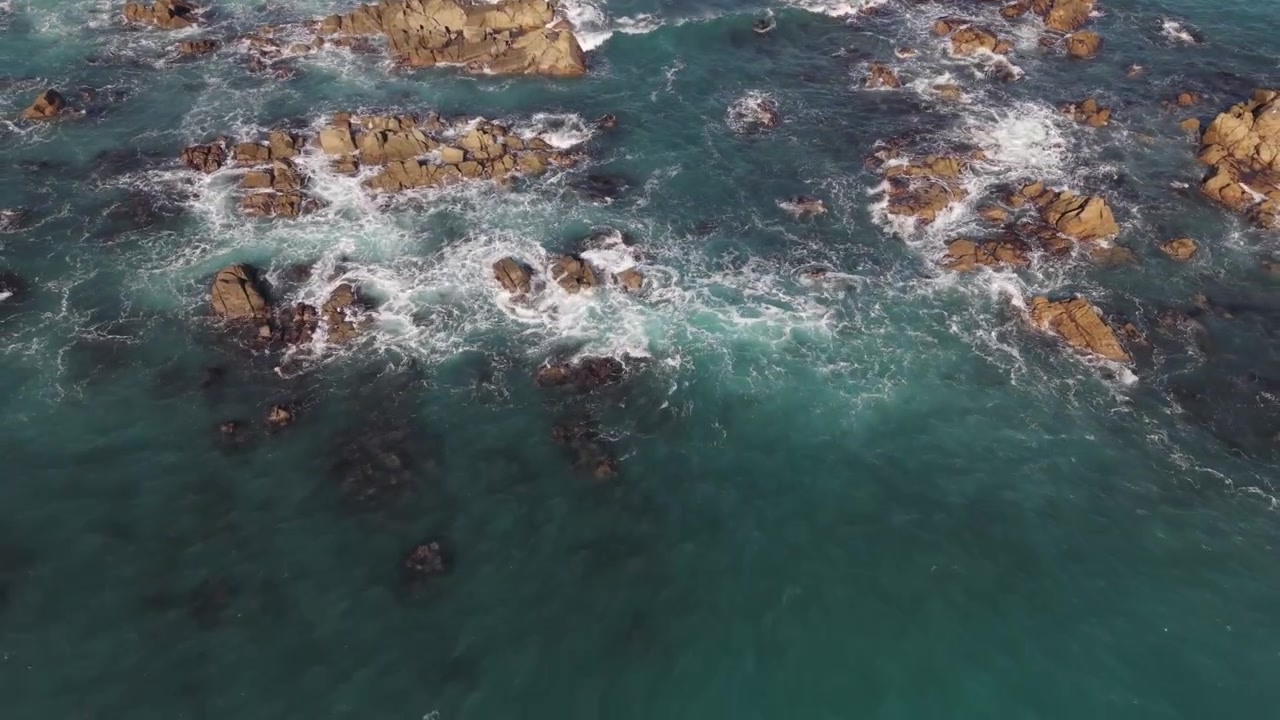 Filmato aereo con drone di affioramenti rocciosi sotto il sole del tardo pomeriggio con onde che si infrangono sulle rocce in un mare blu cristallino e viste sul fondale marino, allontanandosi su acqua limpida