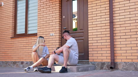 couple enjoying sunny day outside home. two friends sit together on steps outside a brick home, enjoying each other's company in warm weather