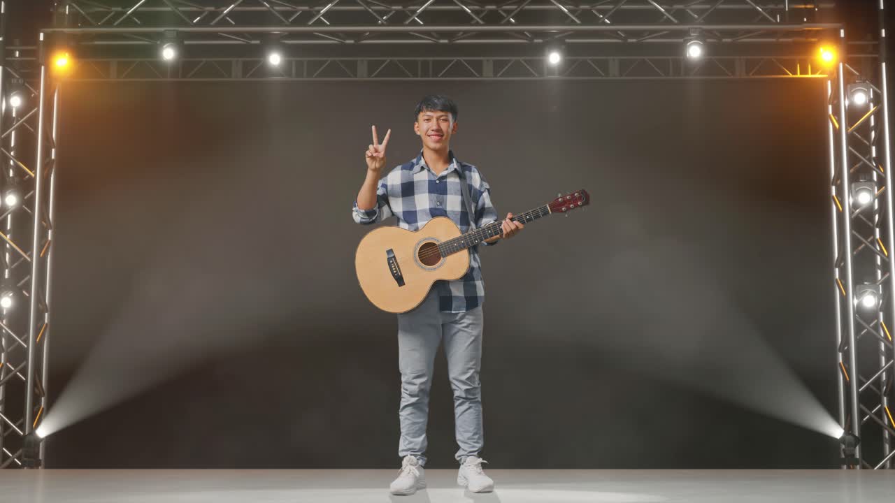 기타를 들고 있는 아시아 청소년의 몸이 가득 차 있어 무대에서 평화와 미소를 짓는 몸짓을 보여준다.