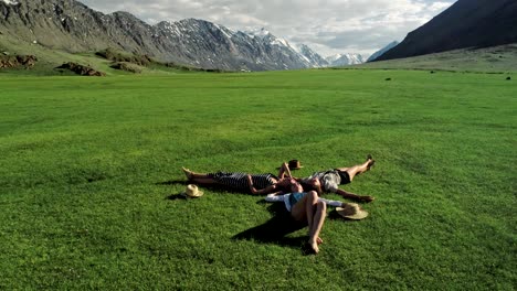 three attractive girls lying on green grass and having fun on a meadow sunny day and background of mountain