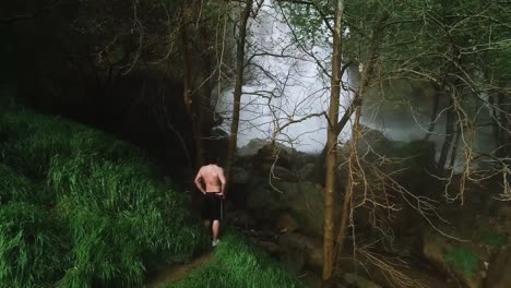 fit adult male watching kfarhelda waterfall through trees in lebanon, aerial