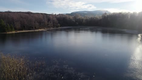 Aerial-drone-footage-flying-over-the-surface-of-a-frozen-loch-and-reeds-in-a-winter-landscape-on-Rothiemurchus-estate-in-Cairngorms-National-Park,-Scotland-with-a-pine-and-birch-forest