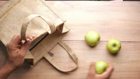 persona poniendo manzanas verdes en una bolsa de compras reutilizable