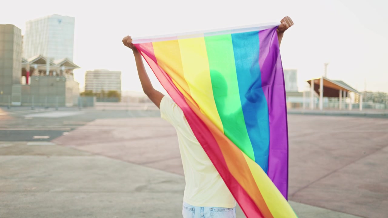 Happy Young Person Waving Rainbow Flag in Urban Setting