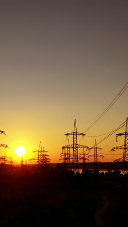 dark electric towers against beautiful sunset. high-voltage electric lines in the evening on red and yellow sky. vertical video
