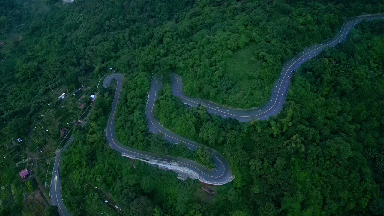 A tilt-down aerial of winding mountain road cutting through dense forest terrain in Tagaytay, Cavite, Philippines