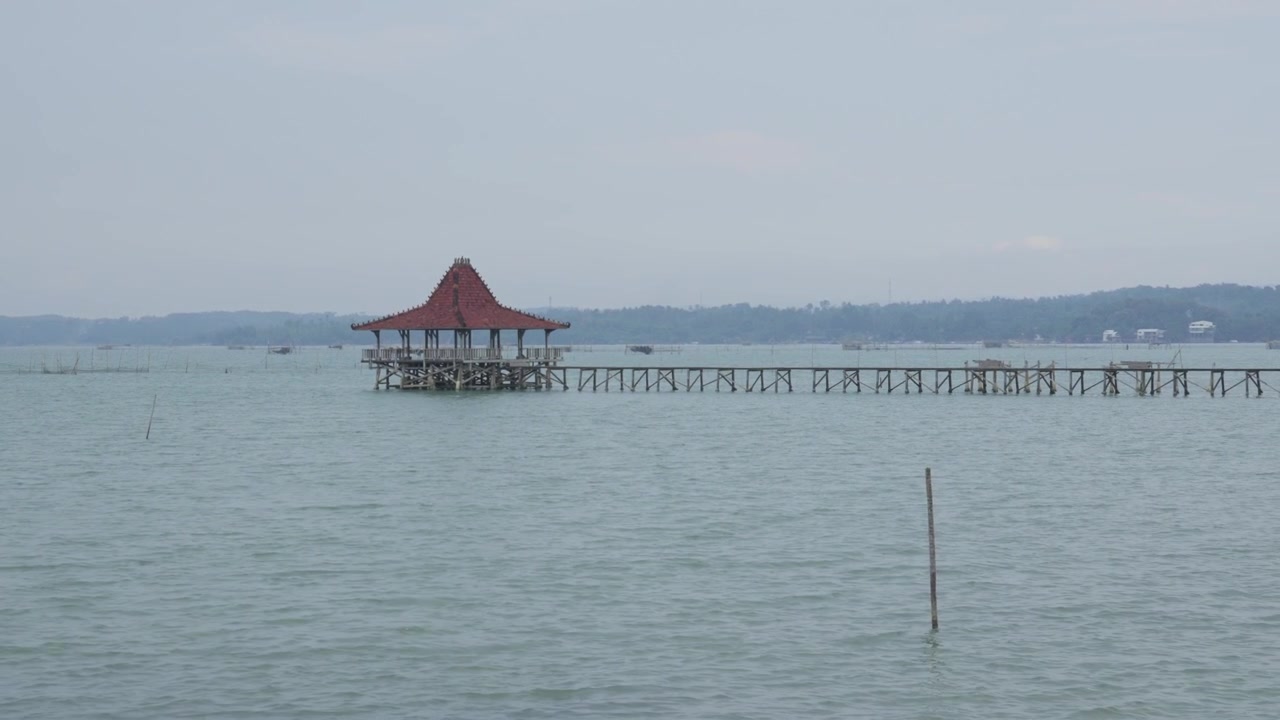 Pemandangan Pesisir: Gazebo Kayu Tradisional di Atas Tiang Pancang dan Lanskap Garis Pantai Berbatu di Indonesia.