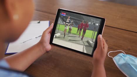 composite of woman sitting at table with face mask, watching rugby match on tablet