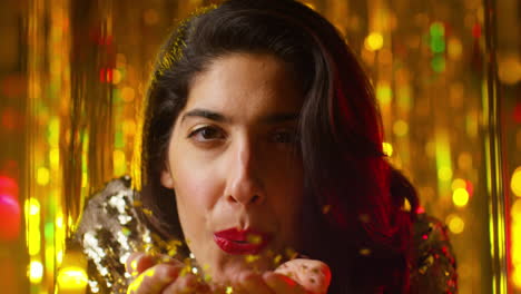 woman celebrating at party or club blowing handful of gold glitter towards camera