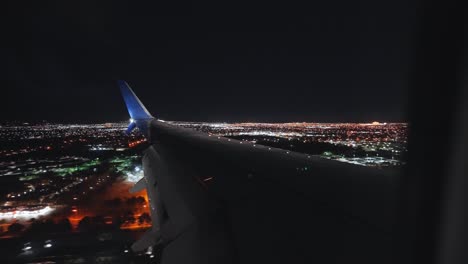 plane landing in an airport next to a city at night from the inside looking outside at the wing