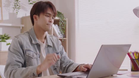 at home, a business asian man types and works online on a desk table with a laptop.