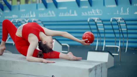 acrobatic woman performing a split with a ball in a park