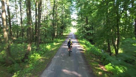 on a sunny summer day, a boy is cycling on a road that passes through a forest on both sides, and he is enjoying the natural surroundings