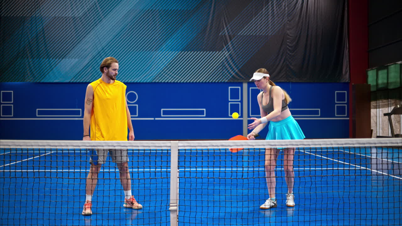 Two men and two women playing pickleball on a blue, inside court
