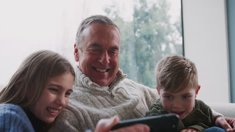 grandfather playing video game with grandchildren on mobile phone at home