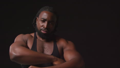 portrait of serious male athlete wearing fitness vest training flexing muscles and preparing psychologically for sports event against black studio background