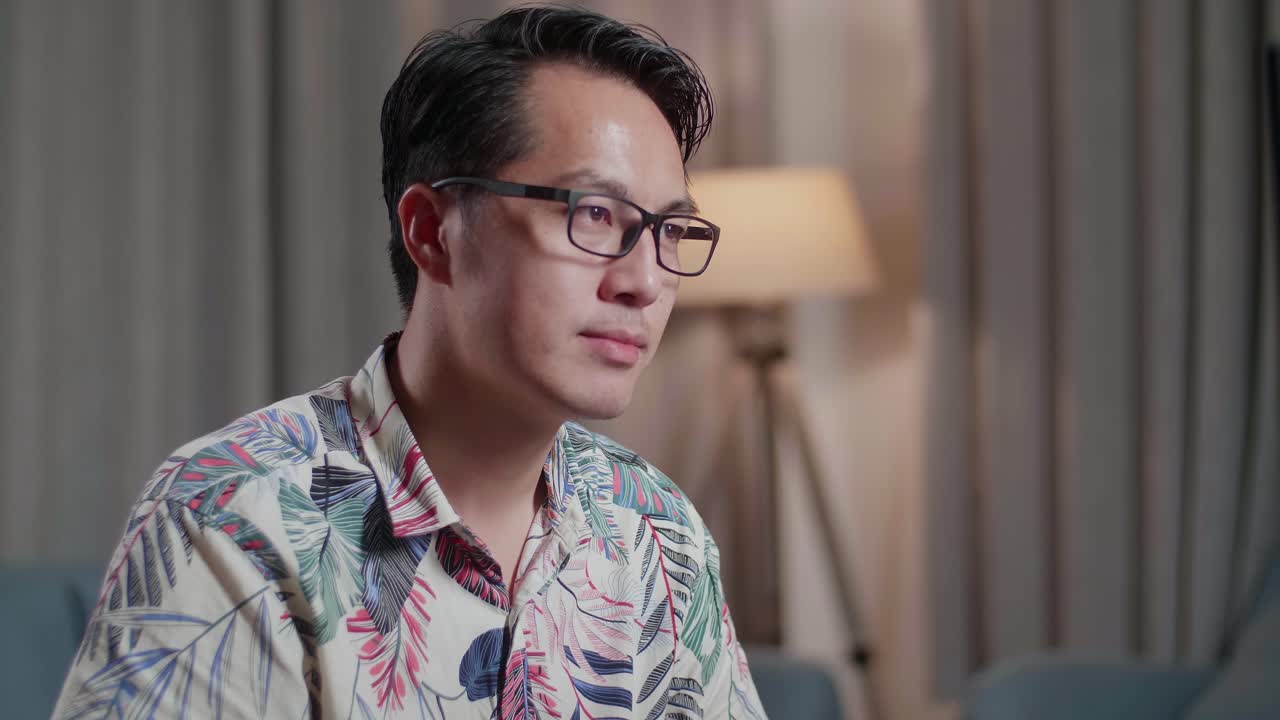 체어에 앉은 아시아인 남자가 집에 있는 카메라 에 있는 데스크에서 비디오를 편집하는 동안 카메라에 미소 짓고 있다.