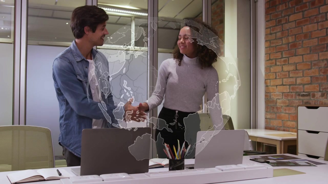 Equipo inclinado sobre laptops, con una superposición de globo terráqueo, señalando y estrechando manos mientras acuerdan una estrategia de negocios