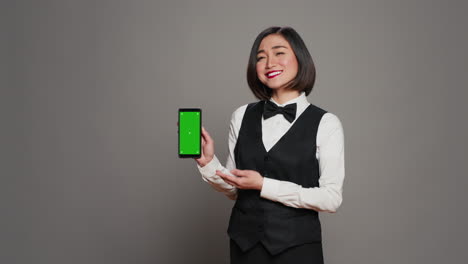 Asiatischer-Hotel-Concierge-Zeigt-Auf-Telefon-Mit-Greenscreen-Layout