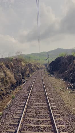 a railway track runs through gentle hills on both sides, with fluffy white cloudy sky maharashtra india 4k