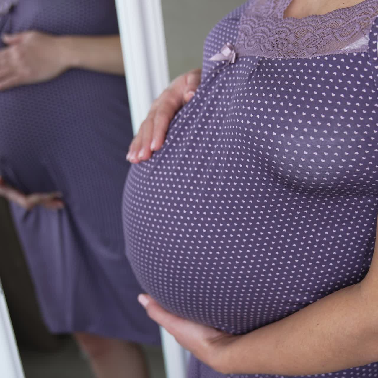 Woman hands touching her tummy, waiting child. Pregnant expectant mother looking at her reflection and stroking her stomach lovingly. Close up shot