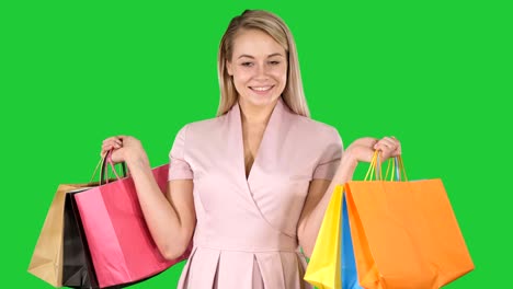 una joven muy emocionada de pie mirando la cámara mostrando bolsas de compras en una pantalla verde, llave de croma