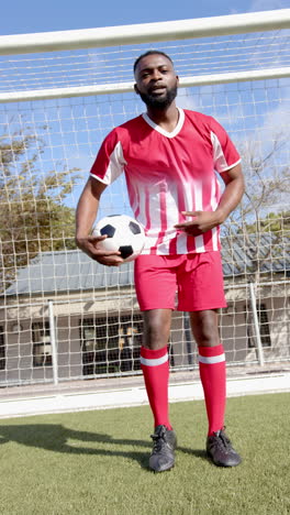 vertical video: soccer player in red uniform holding ball confidently on field