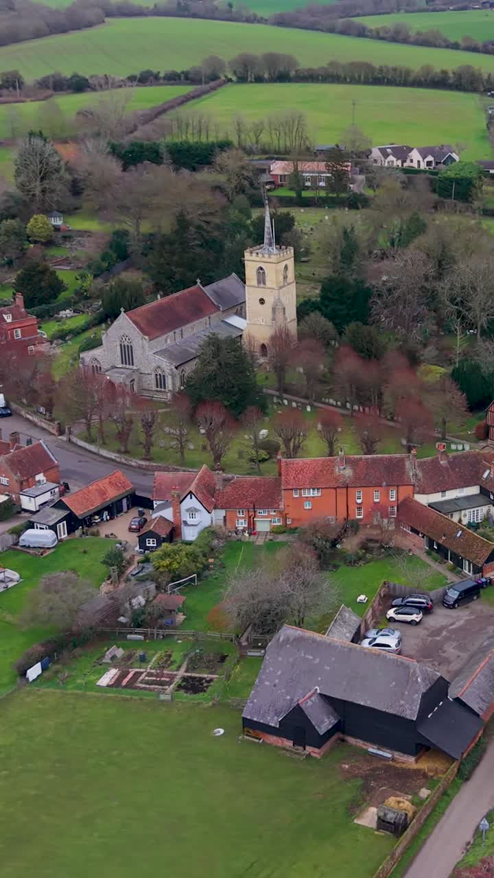 Ripresa verticale con drone che inizia sopra Standon, con rotazione a destra e discesa attorno a una chiesa normanna. La discesa rivela la via principale del paese, i tetti e la campagna circostante con un movimento aereo fluido.