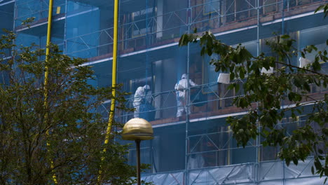 equipo de eliminación de amianto trabajando en la construcción, árboles ondeando en primer plano