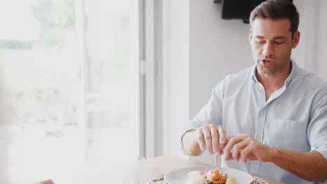 family with senior parents and adult offspring eating meal around table at home together