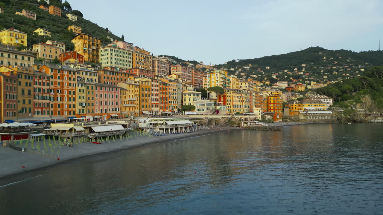 Camogli, a Ligurian coastal town, showcases colorful, densely packed hillside buildings with a serene beachfront and a bustling promenade, captured beautifully from an elevated angle