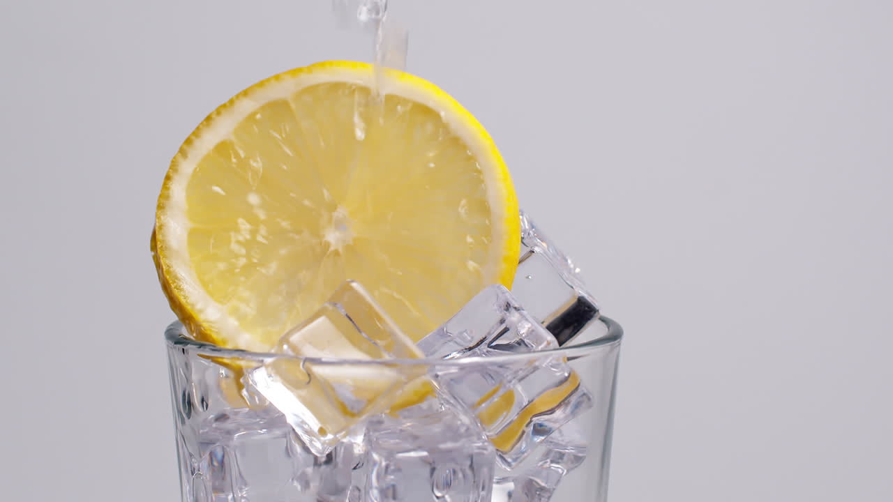 Acqua frizzante fredda e fresca che si versa in un bicchiere con ghiaccio e fette di limone